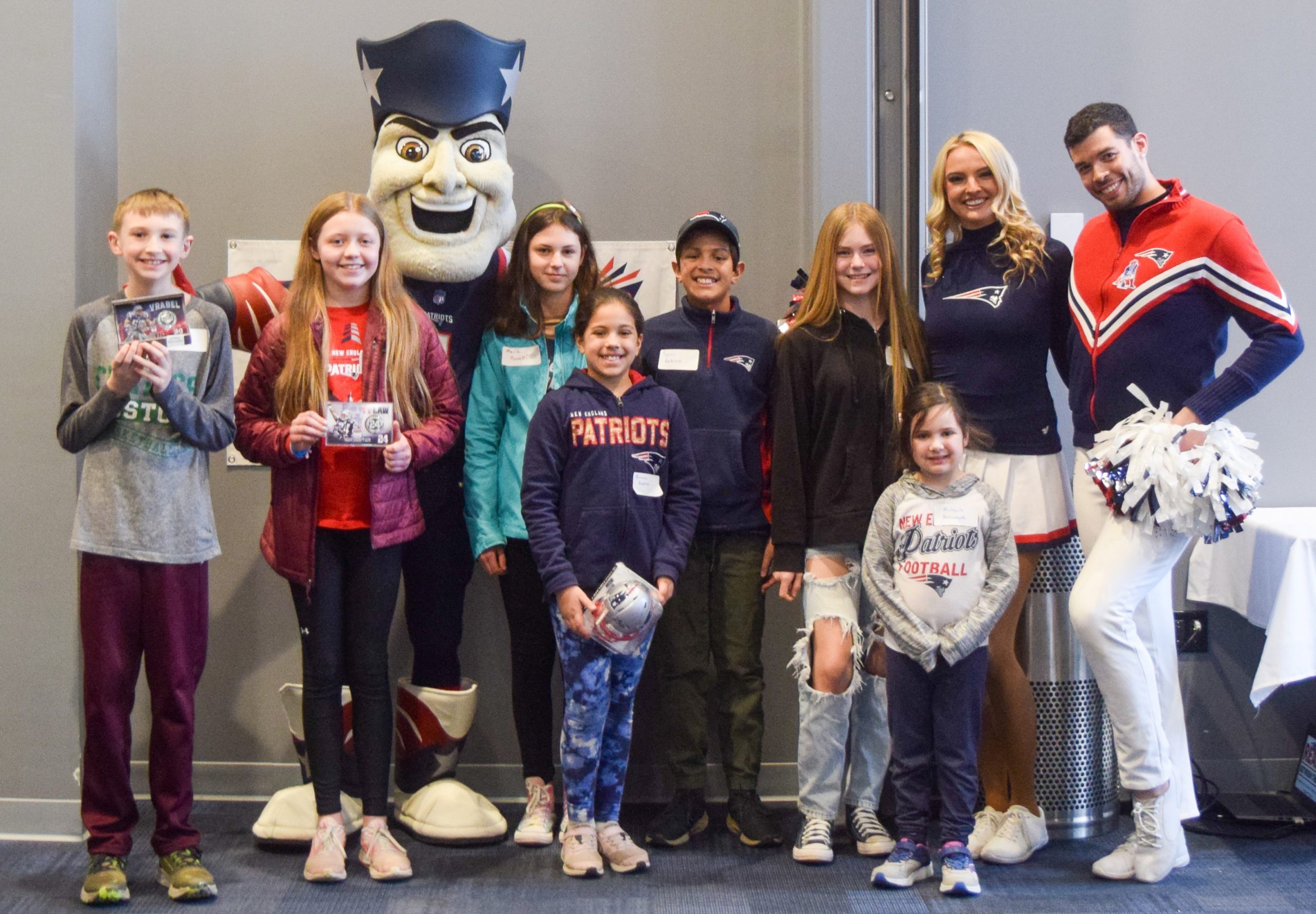 Smiling students pose with their challenge prizes standing with Patriots cheerleaders and mascot